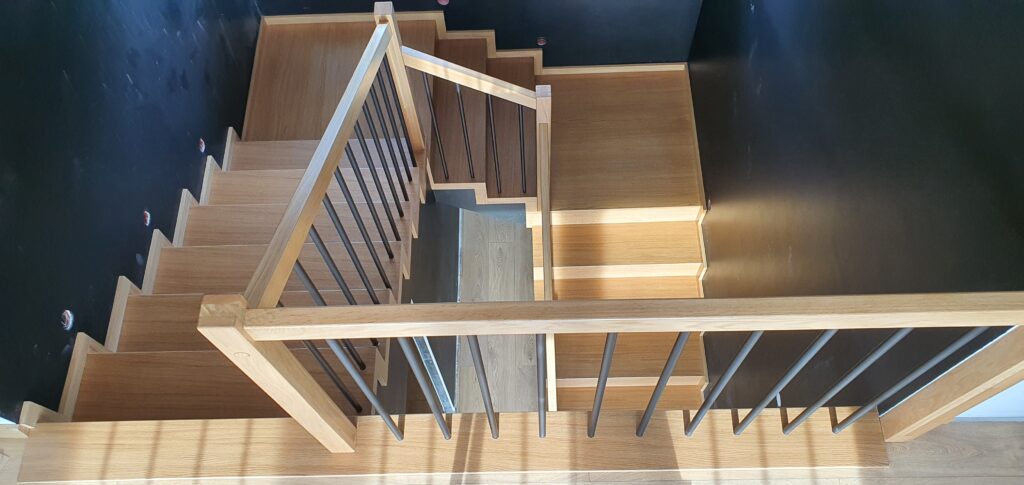 Schody dywanowe dąb natura. Solidna balustrada wypełniona czarnymi rurkami. Realizacja w Tychach