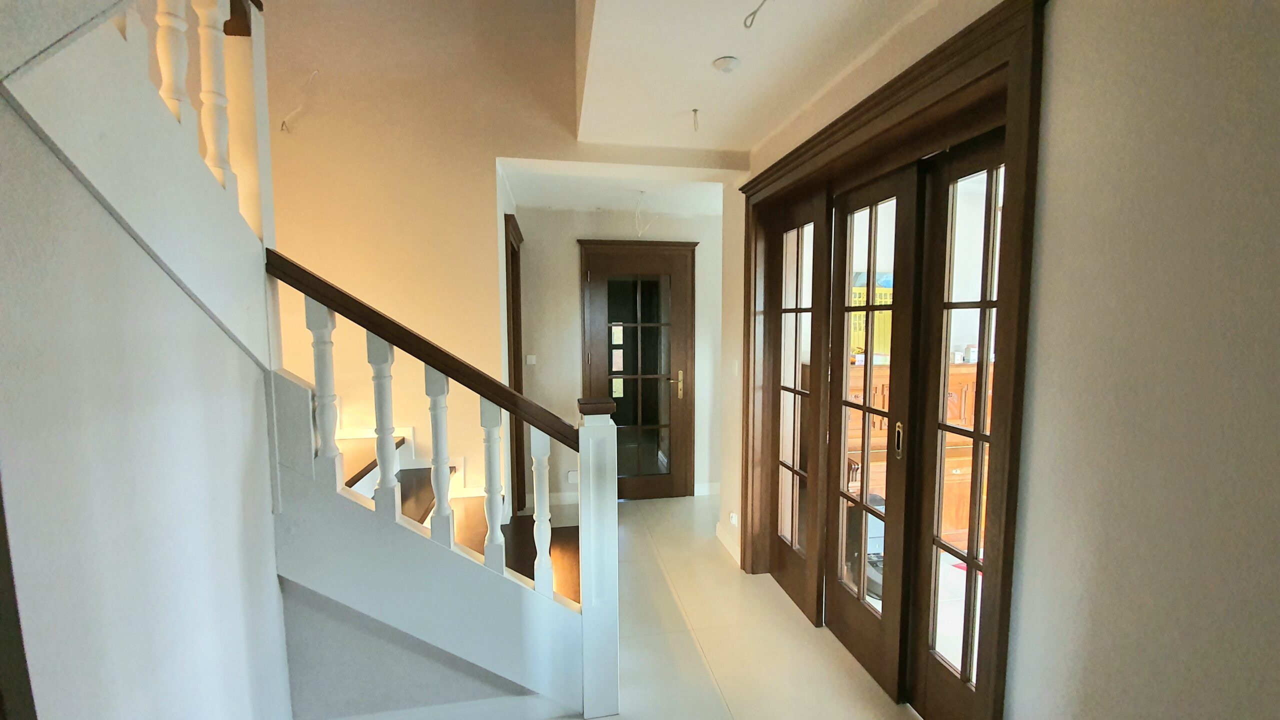 Ekskluzywne schody, oraz drzwi w stylu pałacowym. Drzwi na parterze w kolorze orzech, natomiast na piętrze malowane na biało z widoczną struktura drewna. Realizacja Żernica